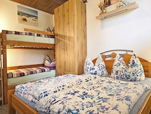 Ein Etagenbett mit unterem Bett, ein Holzschrank, ein Bett mit blumigem Überwurf und ein Regal mit Dekoration.