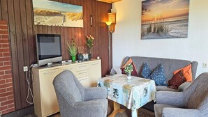 Een knus ogende kamer met een houten wand, een televisie, een tafel met een sprei en een bank met decoratieve kussens.
