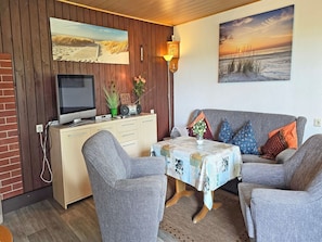 Ein gemütliches Zimmer mit einer Holzwand, einem Fernseher, einem Tisch mit einer Patchworkdecke und einer Couch mit gemusterten Kissen.