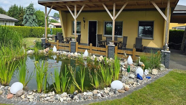 Een gebouw met een overdekt terras, buitenmeubilair en een vijver met decoratieve details.