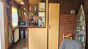 Een kleine leefruimte met een kitchenette, een houten deur, een grijze bank en een bakstenen muur.