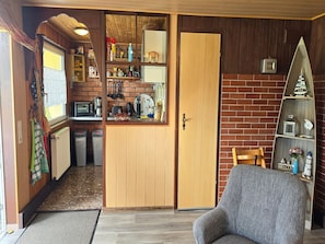 Ein kompakter Wohnbereich mit Küchenzeile, einer Holztür, einem grauen Sofa und einer Ziegelwand.