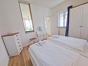 Ein Schlafzimmer mit zwei Betten, einem Schminktisch, einem Frisiertisch und einem Fenster mit Vorhängen.