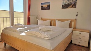 Un letto matrimoniale con lenzuola bianche, una testiera in legno, un comodino con cassetti e due quadri appesi al muro.