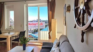 Un soggiorno con divano, tavolo da pranzo, una pianta in vaso, vista sul mare e un cartello con scritto 'Kutterfisch'.