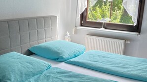Ein Doppelbett mit grau gepolstertem Kopfteil, zwei passende Kissen und ein Fenster mit Blick auf Grünflächen.