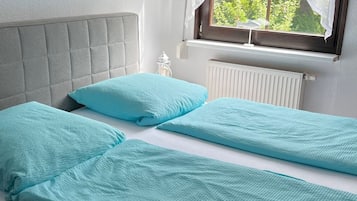 Ein Doppelbett mit grau gepolstertem Kopfteil, zwei passende Kissen und ein Fenster mit Blick auf Grünflächen.