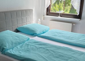 A twin bed with a grey upholstered headboard, two matching pillows, and a window with a view of greenery. - Stockrose vacation apartment - very close to the Jasmund National Park (Lohme OT Nipmerow)