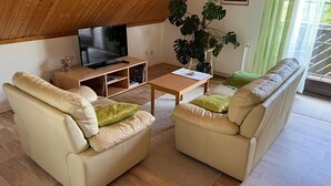 Ein Wohnzimmer mit Fernseher, zwei Sofas, einem Couchtisch und einer großen Pflanze.