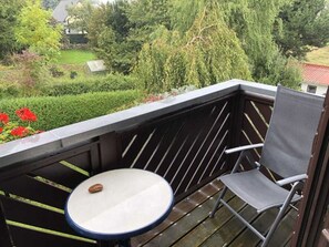 A balcony with a table and a chair, surrounded by greenery and a house in the background. - Stockrose vacation apartment - very close to the Jasmund National Park (Lohme OT Nipmerow)