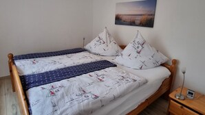Een bed met een sprei en kussens met een nautisch thema, een nachtkastje met een lamp en een aan de muur hangend schilderij.