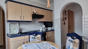 Een kleine keuken met een magnetron, waterkoker en koffiezetapparaat, een tafel met placemat en een stoel met placemat.
