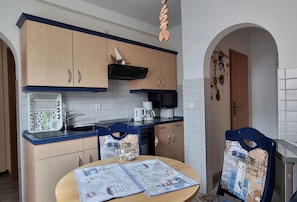 A compact kitchen with a microwave, kettle, and coffee maker, a table with a placemat, and a chair with a placemat. - Vacation apartment Kollwitz - very close to the Sassnitz town harbor - Holiday apartment (Sassnitz auf Rügen)