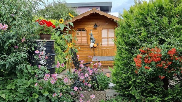 Een houten chalet met een tuin ervoor, omgeven door diverse planten en bloemen.
