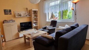 Een woonkamer met een bank, televisie, planken en een raam met uitzicht.