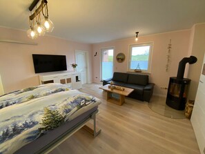 A cozy room with a bed, a sofa, a TV, and a fireplace. - Vacation apartment Tiny - on the edge of the national park in Hagen - Ferienwohnung Tiny - (Lohme OT Hagen)