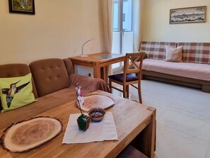 A living room with a brown sofa, a wooden dining table with a vase and a wooden bowl, and a pink sofa in the background. - Vacation home Zum Kreideblick, FeWo Seeigel (Sassnitz auf Rügen)