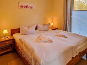 A neatly made bed with pillows and a blanket, a bedside table with a lamp, and a wall-mounted picture. - Vacation home Zum Kreideblick, FeWo Seeigel (Sassnitz auf Rügen)