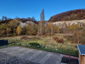 A paved area with a fence, a wooden structure, and a natural landscape with trees and a hill. - Vacation home Zum Kreideblick, FeWo Seeigel (Sassnitz auf Rügen)