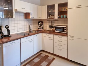 A compact kitchen with white cabinets, a stainless steel sink, a microwave, and a coffee maker. - Vacation home Zum Kreideblick, FeWo Seeigel (Sassnitz auf Rügen)