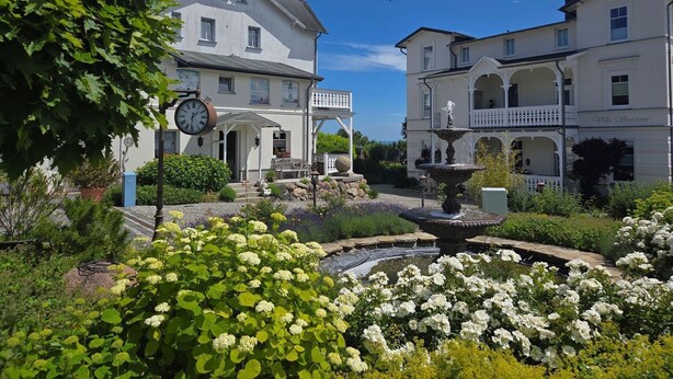 Un edificio storico con una torre dell'orologio, una fontana e un giardino con fiori bianchi.
