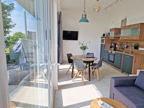 A modern kitchen with a dining area, a sofa, and a view through a glass door. - Villa Küstenperle, App. Muschelblick - pure sea view! (Sassnitz auf Rügen)