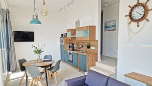 Moderni keittiö, jossa on puiset kaapit, ruokailutila pöydän ja tuolien kera, sohva ja seinälle kiinnitetty kello.