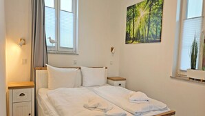 Makuuhuoneessa on sänky, yöpöydät, yölamppu, ikkuna, jossa on sälekaihtimet, seinään kiinnitetty valaisin ja taulu.