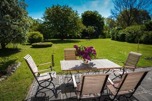 An outdoor seating area with a table and chairs, surrounded by a well-maintained garden and trees. - Jasmundhus on Rügen - Holiday apartment Backbord (Neddesitz auf Rügen)