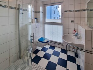 Ein Badezimmer mit Schachbrettboden, einer Toilette mit blauem Sitz, einem Waschbecken und einer Dusche.