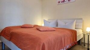 Ein Bett mit weißem Kopfteil, zwei Kissen und einer roten Decke.