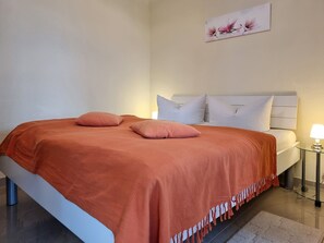 Ein Bett mit weißem Kopfteil, zwei Kissen und einer roten Decke.