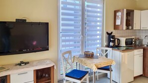 Eine kompakte Küche mit Mikrowelle, Kaffeemaschine und kleinem Kühlschrank. Es gibt eine Essecke mit Tisch und Stühlen sowie einen an der Wand befestigten Fernseher.