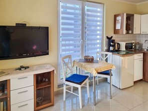 Eine kompakte Küche mit Mikrowelle, Kaffeemaschine und kleinem Kühlschrank. Es gibt eine Essecke mit Tisch und Stühlen sowie einen an der Wand befestigten Fernseher.