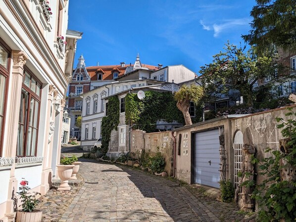 A cobblestone street with buildings on either side, including a white building with a balcony and a red-roofed building in the background. - Small fisherman's hut - rustic vacation home by the sea - Small fisherman's hut - rustic and (Sassnitz auf Rügen)