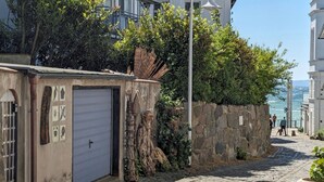 Una calle adoquinada con un muro de piedra, una reja metálica y un edificio de fachada blanca.