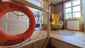 Una habitación con techo de madera, una silla amarilla, un radiador blanco y una puerta con un salvavidas colgado.