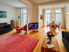 Ein modernes Wohnzimmer mit Flachbildfernseher, einem roten Sofa, einem Holzesstisch und einem Balkon mit Vorhängen.