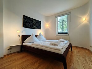 Ein Schlafzimmer mit einem Bett, Nachttischlampen, einem Fenster und einem Wandbild.