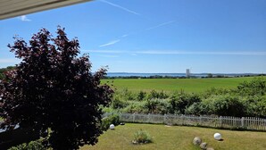 A view of a grassy yard with a tree, a white fence, and a distant structure. - Villa Meerzeit - Holiday apartment Mare Azur (Sassnitz)