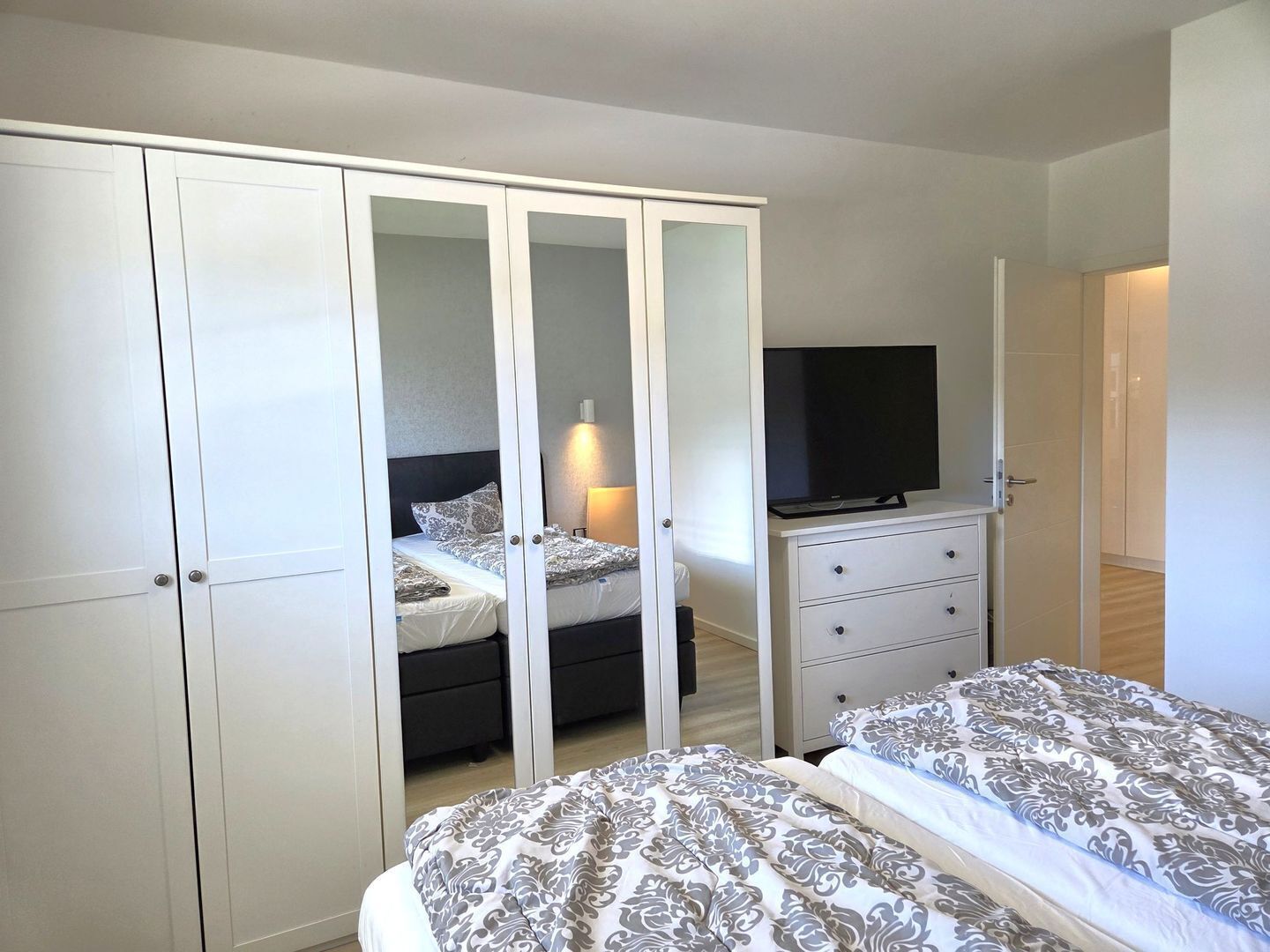 A bedroom with a wardrobe, a TV, two beds, and a bedside table.