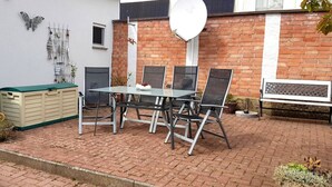 Un patio con una mesa y sillas, un banco, una antena parabólica y adornos en una pared de ladrillo.