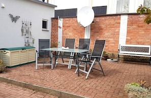 Eine Terrasse mit Tisch und Stühlen, einer Bank, einer Satellitenschüssel und Dekoration an einer Ziegelwand.