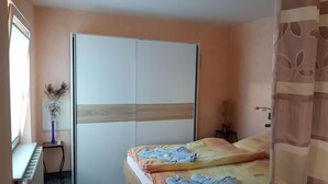 Un dormitorio con cama, un armario, un radiador, una mesita con un florero y una planta en maceta.