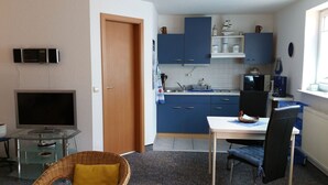 Cocina compacta con armarios azules, microondas, tostadora y un comedor con una silla y mesa.