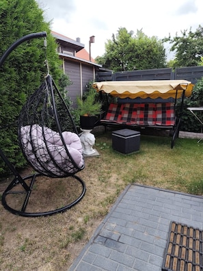 A hanging chair with cushions, a covered outdoor seating area, and a small statue. - Dornbusch vacation apartment - quiet location on the outskirts - Dornbusch vacation apartment - in (Sassnitz auf Rügen)