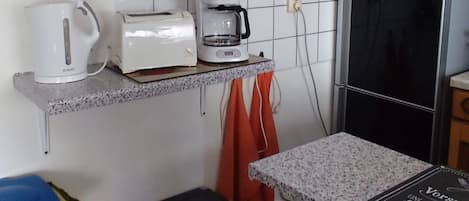 A kitchen with a wooden cabinet, a coffee maker, a toaster, a clock, a refrigerator, and a trash bin.
