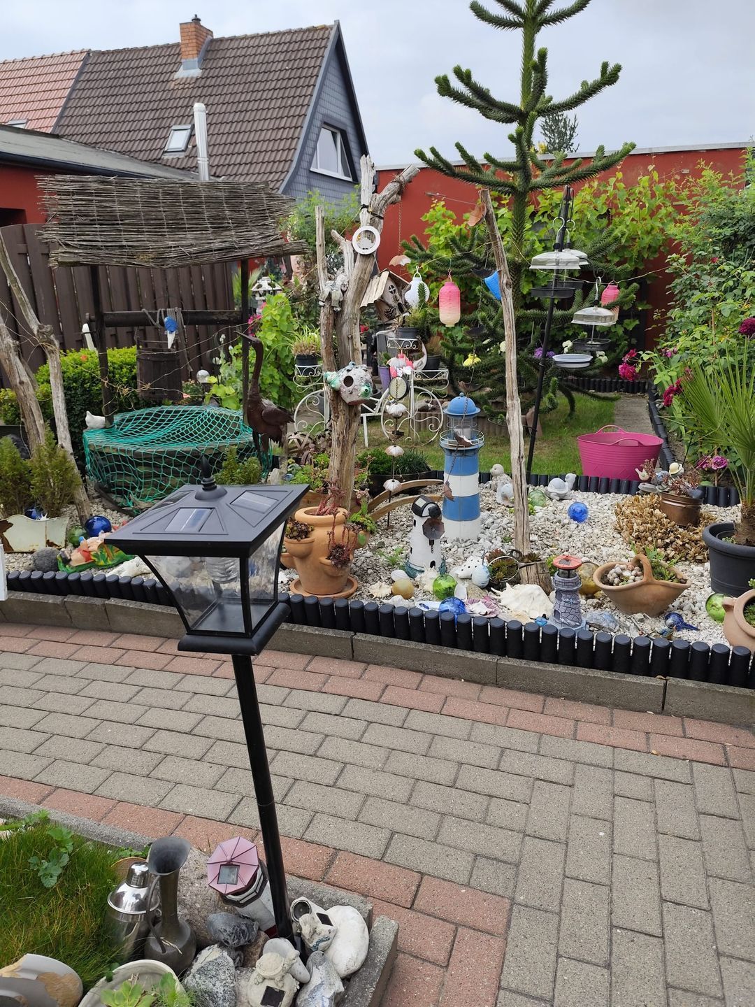 A garden with a variety of plants, a bird feeder, and a decorative fence.