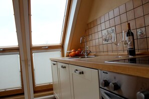 Eine Küche mit Fenster, Spüle, einer Weinflasche und einer Obstschale.