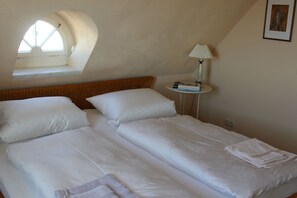 Ein Schlafzimmer mit zwei Betten, einem Oberlicht, einer Nachttischlampe und einem kleinen Tisch mit Büchern.